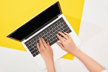 sarı ve beyaz arka planda dizüstü bilgisayar kullanan kadının kırpılmış görünümü