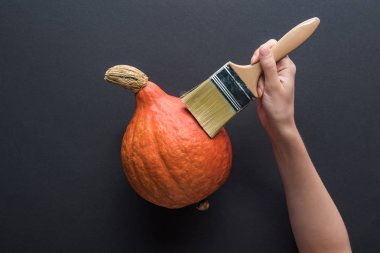 siyah arka plan üzerinde balkabağı yakınında paintbrush tutan kadın kısmi görünümü