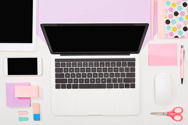 flat lay with laptop, digital tablet, smartphone with blank screen, office supplies and computer mouse on violet and white background