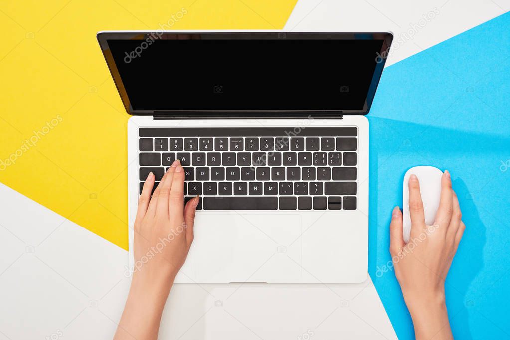 cropped view of woman using laptop with blank screen and computer mouse on yellow, blue and white background