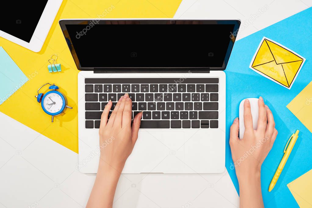 cropped view of woman using laptop near office supplies and mail icon on yellow, blue and white background