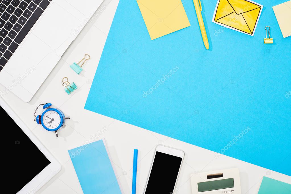 top view of laptop, smartphone, digital tablet with blank screen and office supplies on blue and white background