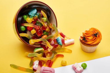 sarı arka plan üzerinde cupcake yakın kase dağınık renkli sakızlı tatlılar, Halloween tedavi