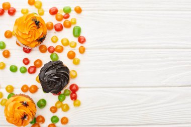 kopya alanı ile beyaz ahşap masa üzerinde renkli bonbon ve cupcakes üst görünümü, Halloween tedavi