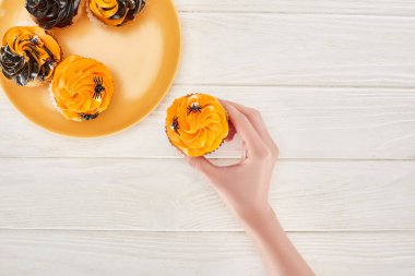 beyaz ahşap masa üzerinde turuncu plaka örümcekler ile lezzetli cupcake alarak kadın kırpılmış görünümü, Cadılar Bayramı tedavi