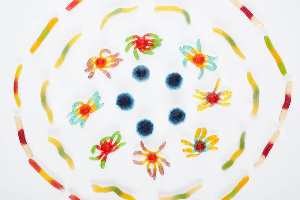 top view of colorful gummy spiders and worms in circle isolated on white, Halloween treat