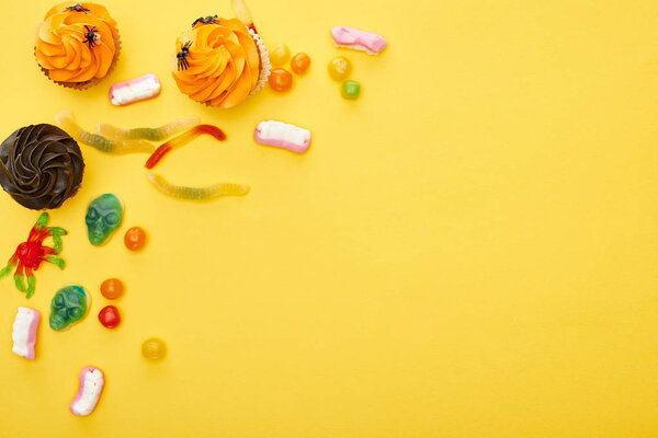 top view of colorful gummy sweets and cupcakes on yellow background, Halloween treat