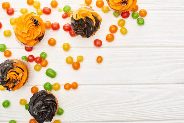 top view of colorful bonbons and cupcakes on white wooden table, Halloween treat