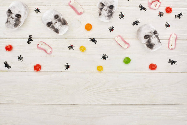 top view of bonbons, gummy teeth, skulls and spiders on white wooden table, Halloween treat