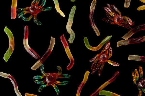 top view of colorful gummy spiders and worms isolated on black, Halloween treat