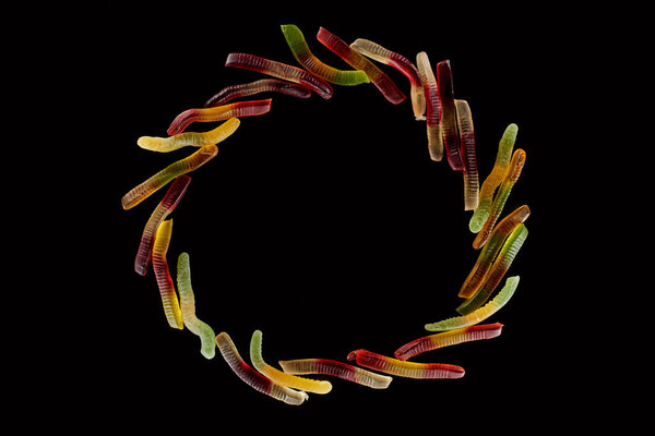 top view of round frame made of colorful gummy worms isolated on black, Halloween treat
