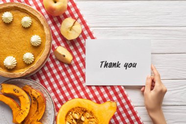 elma ile ahşap beyaz masada kabak pasta yakınında teşekkür kartı tutan kadın kırpılmış görünümü