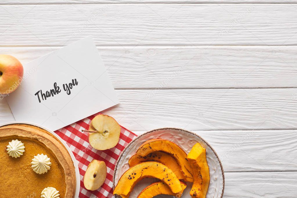 top view of delicious pumpkin pie with thank you card on wooden white table with apples