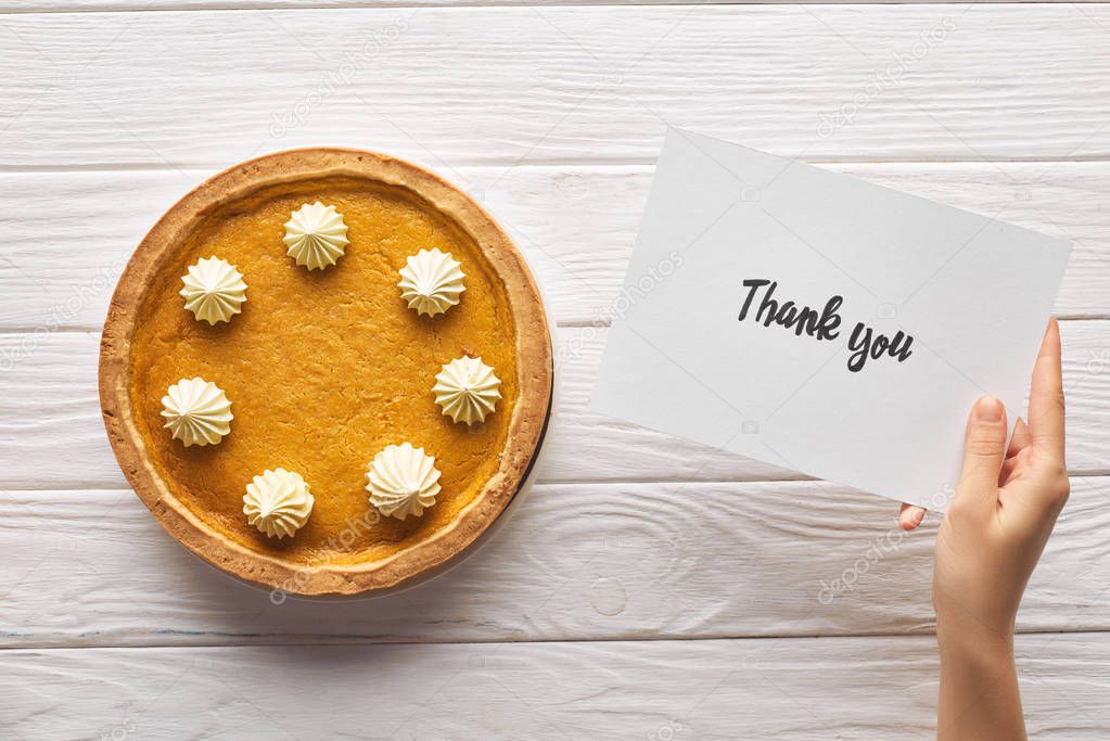 cropped view of woman holding thank you card near pumpkin pie on wooden white table