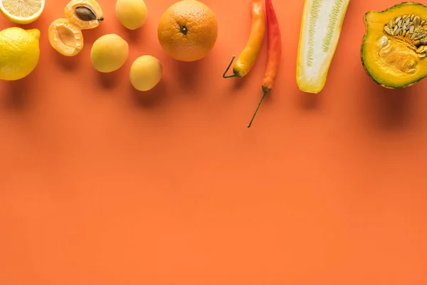 top view of yellow fruits and vegetables on orange background with copy space