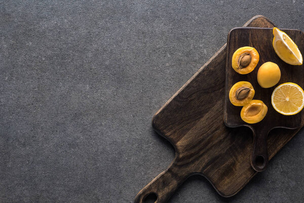 top view of yellow lemons and apricots on wooden cutting boards on grey textured background with copy space