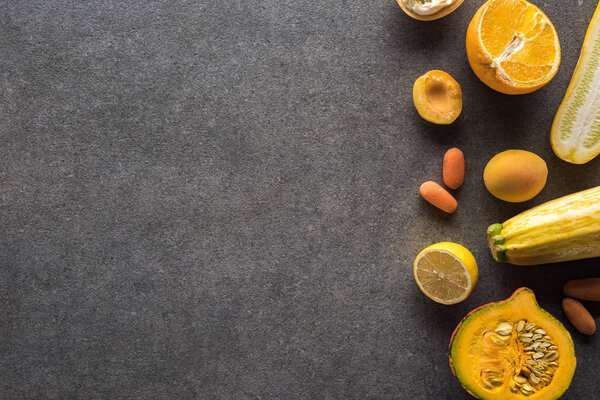 top view of yellow fruits and vegetables on grey textured background with copy space