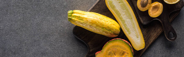 top view of yellow apricots and vegetables on wooden cutting boards on grey textured background, panoramic shot