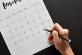 Ausgeschnittene Ansicht einer Frau, die das Datum des Black Friday im Kalender auf schwarzem Hintergrund markiert