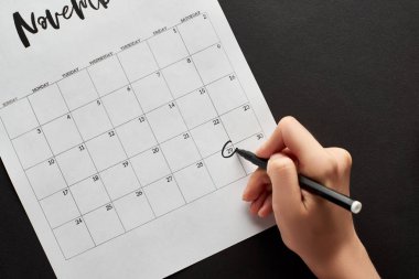 cropped view of woman marking black Friday date in calendar on black background clipart