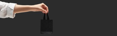 Elinde küçük siyah alışveriş çantasıyla siyah panoramik kareye izole edilmiş bir kadın görüntüsü.