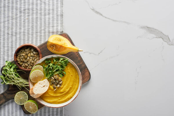 top view of autumnal mashed pumpkin soup on wooden cutting board on marble surface