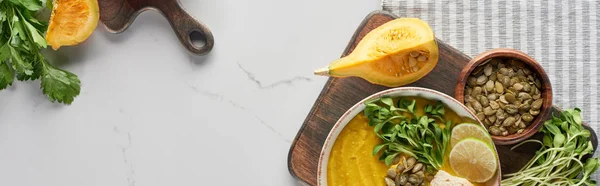 top view of autumnal mashed pumpkin soup on wooden cutting board on marble surface, panoramic shot