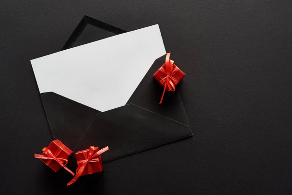 top view of blank card in envelope near presents on black background
