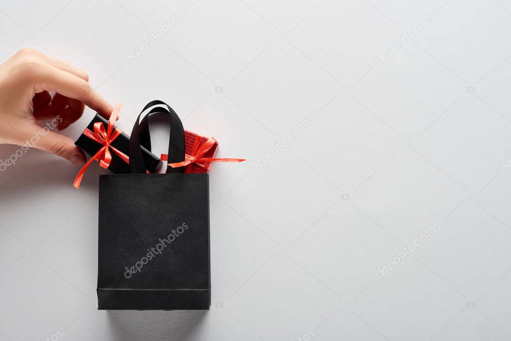 cropped view of woman putting small gift boxes in black shopping bag on white background