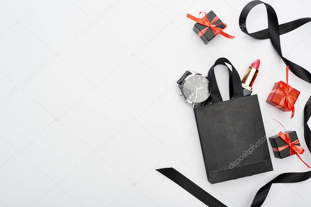 top view of small shopping bag with male wristwatch and female lipstick near ribbon and presents on white background