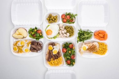 Elma, sebze, et, kızarmış yumurta ve beyaz arka planda salata içeren ekolojik paketlerin üst görünümü 