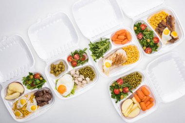 Elma, sebze, et, kızarmış yumurta ve beyaz arka planda salata içeren ekolojik paketlerin üst görünümü 