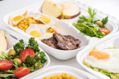 Beyaz arkaplanda elma, sebze, et, kızarmış yumurta ve salata içeren ekolojik paketlerin seçici odak noktası 