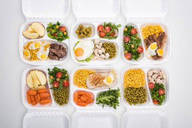 Elma, sebze, et, kızarmış yumurta ve beyaz arka planda salata içeren ekolojik paketlerin üst görünümü 