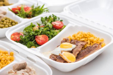 Beyaz arka planda mısır, et, sahanda yumurta ve salata içeren ekolojik paketin seçici odak noktası 