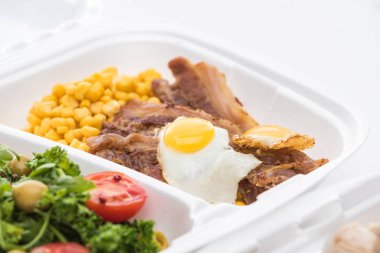 Beyaz arka planda mısır, et, sahanda yumurta ve salata içeren ekolojik paketin seçici odak noktası 