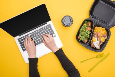 Kadının mısır, et, yumurta ve salata eşliğinde dizüstü bilgisayar ve ekolojik paket kullanması, sarı bardakta izole edilmiş kağıt bardak. 