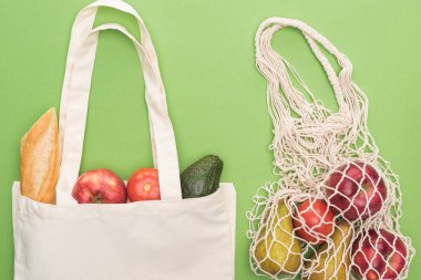 top view of fresh baguette, vegetables and fruits in cotton and string bag isolated on green clipart