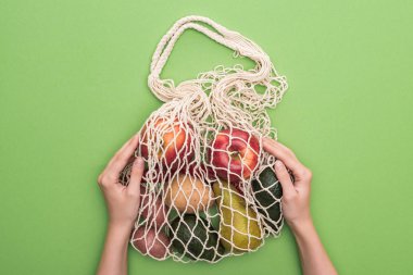 top view of woman holding vegetables and fruits in string bag isolated on green clipart