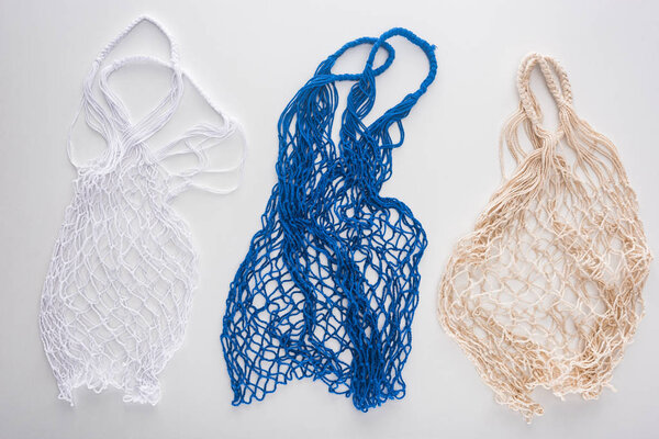 top view of eco friendly white, blue and beige string bags isolated on white