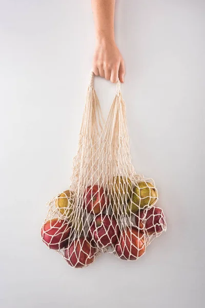 リンゴと梨が白で隔離されたエコフレンドリーなストリングバッグを持つ女性のトリミングビュー — ストック写真