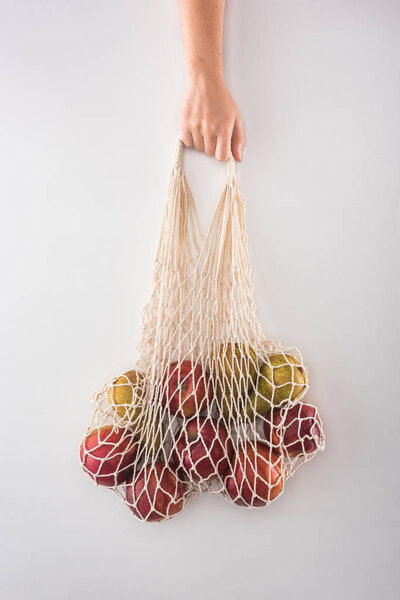 cropped view of woman holding eco friendly string bag with apples and pears isolated on white