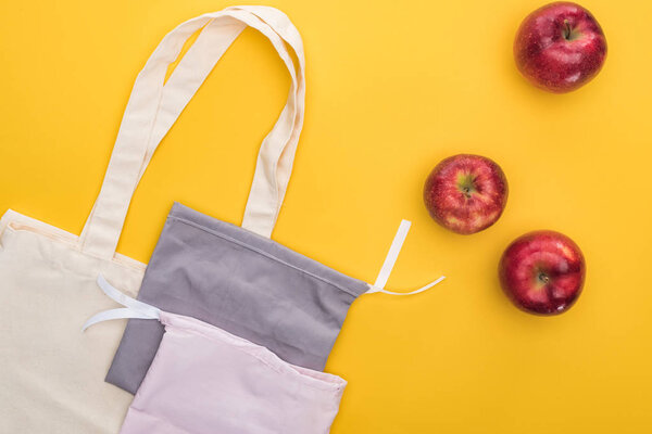 top view of ripe apples near eco friendly bags isolated on yellow