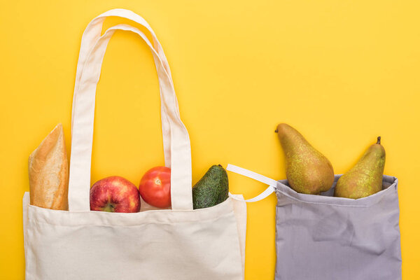 top view of ripe fruits, vegetables and baguette in eco friendly bags isolated on yellow