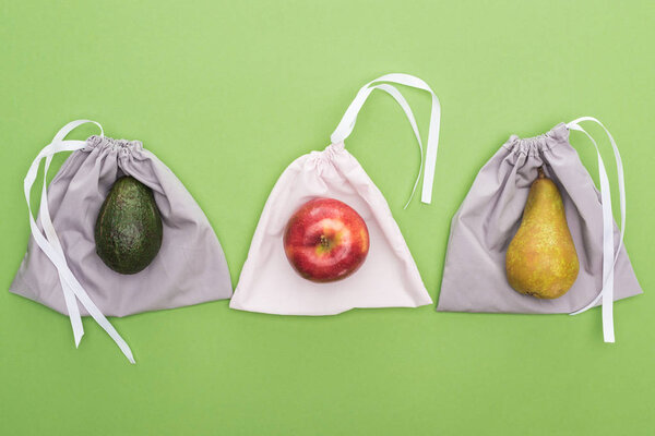 top view of avocado, pear and apple on eco friendly bags isolated on green