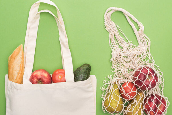 top view of fresh baguette, vegetables and fruits in cotton and string bag isolated on green