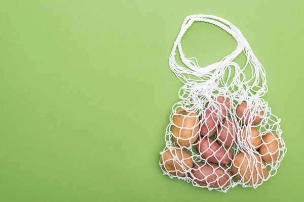緑に隔離された環境に優しいストリングバッグの新鮮なジャガイモのトップビュー — ストック写真