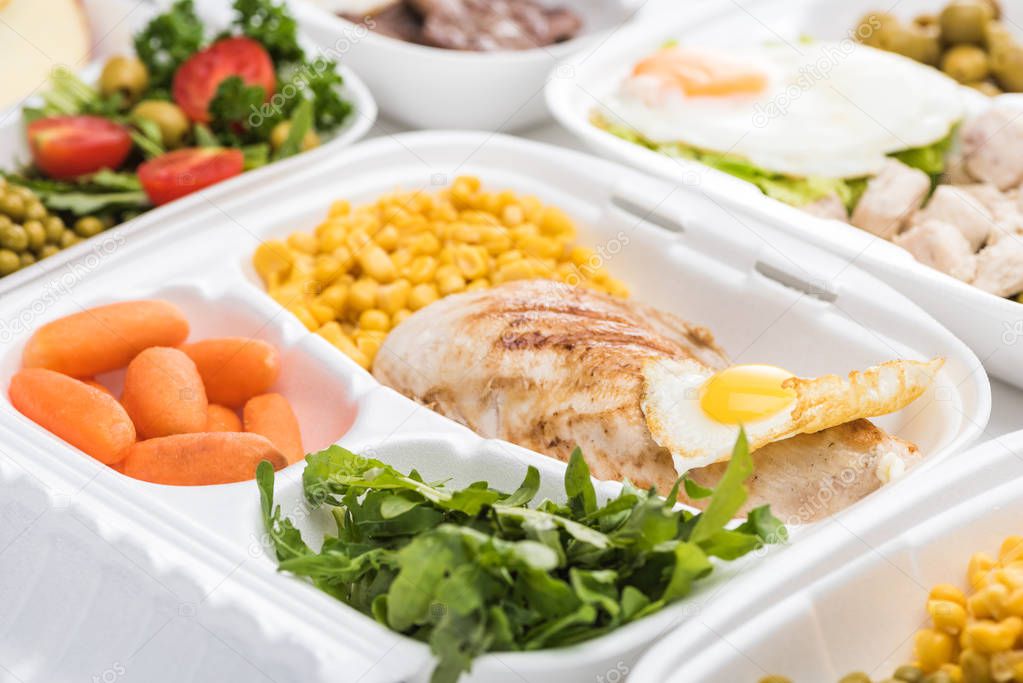 selective focus of eco package with vegetables, meat, fried egg and arugula on white background 