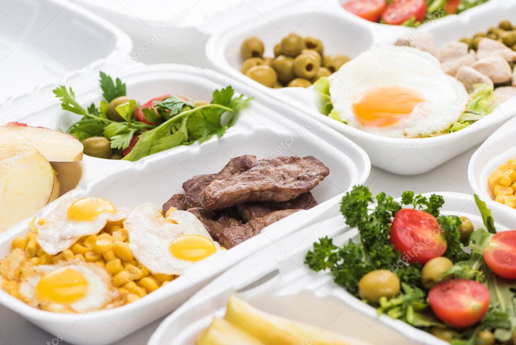 selective focus of eco package with salad, apples, fried eggs and meat on white background 