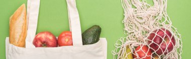 top view of fresh baguette, vegetables and fruits in cotton and string bag isolated on green, panoramic shot clipart